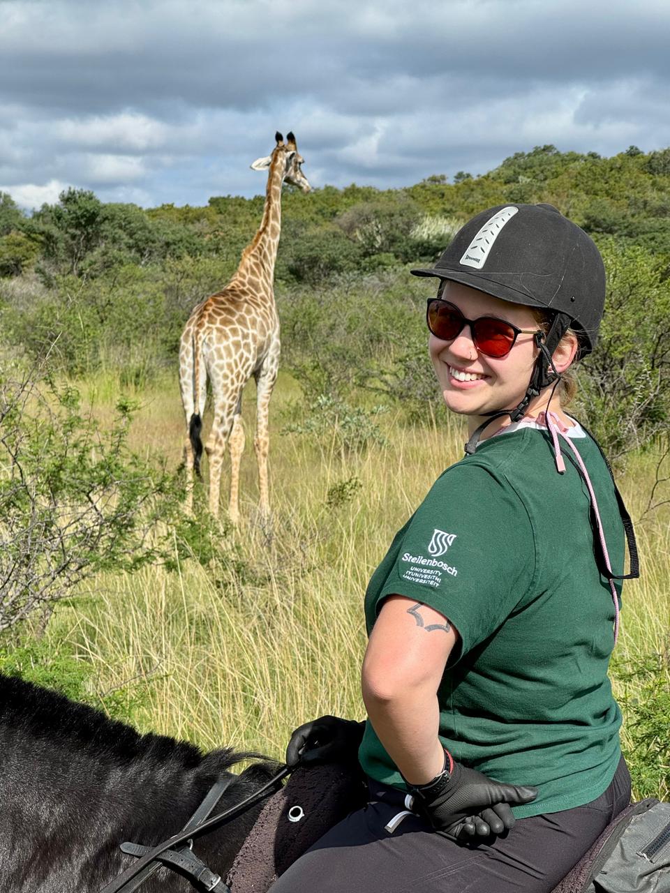 Daughter on horseback in the African bush with a giraffe in the distance