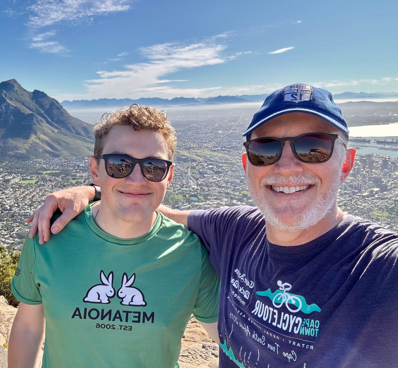 Father and adult son taking a selfie on Lion's Head with Cape Town and the ocean spread out behind