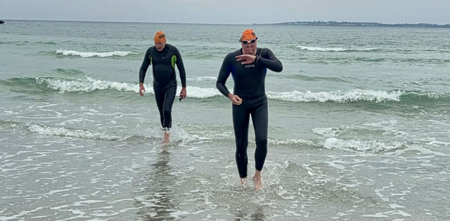 Two swimmers walking out of the surf onto the beach at the end of the crossing
