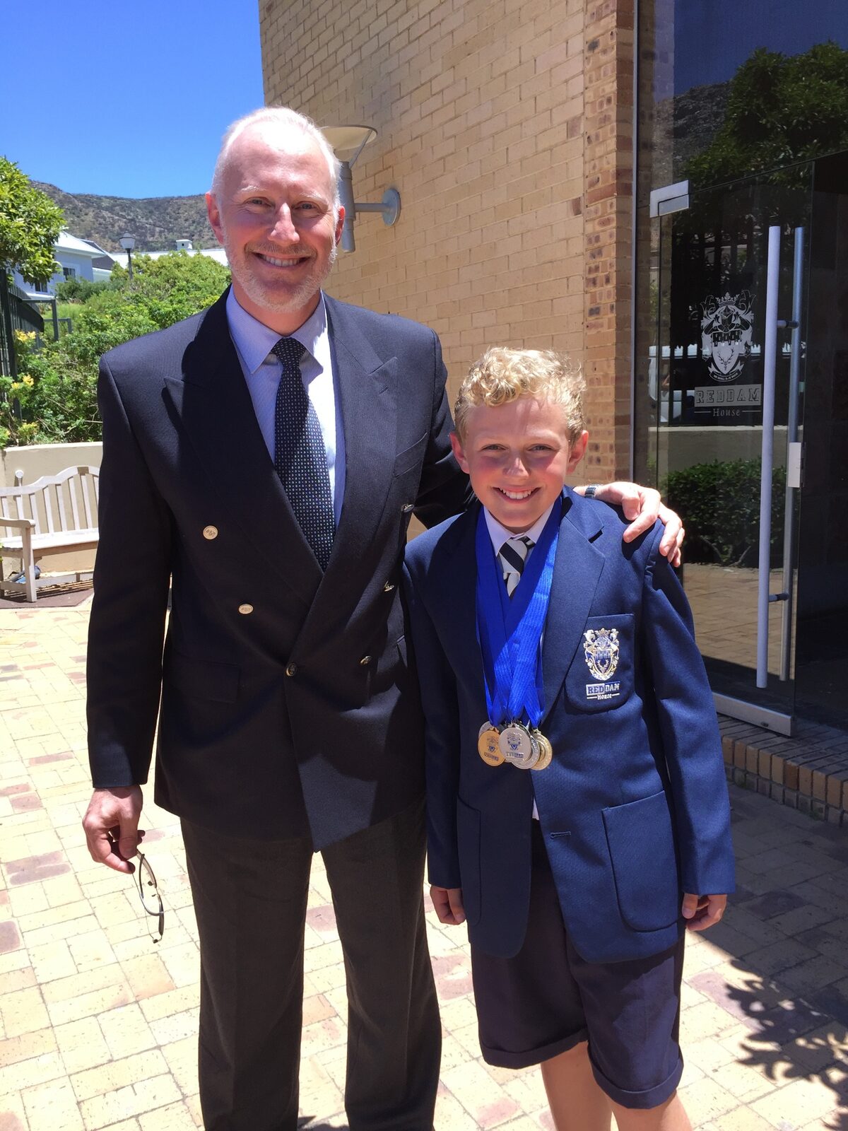 Young boy in school blazer with medals standing beside his father at Reddam House