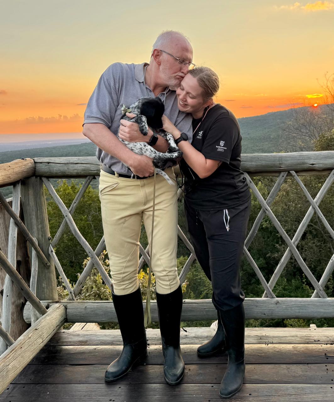 Father kissing his daughter on the forehead at sunset, holding a puppy