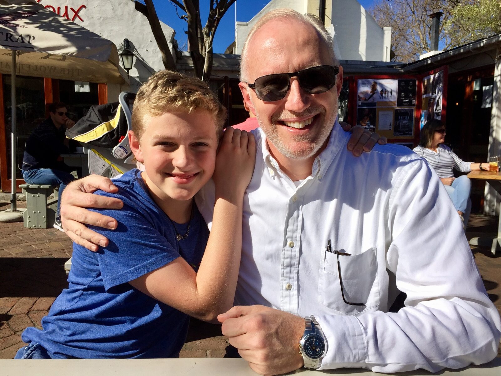 Young son with his arm around his smiling father at an outdoor cafe table