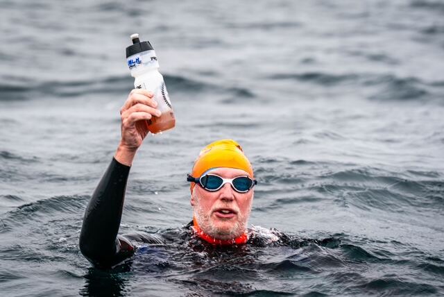 Swimmer pausing in the water to take a feed from a bottle handed over from the boat