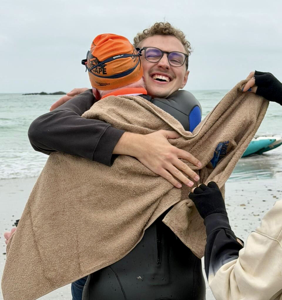 Swimmer being embraced by his son on the beach after finishing the swim