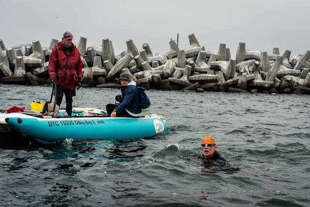 Swimmer entering the cold water beside the support boat at the harbour wall