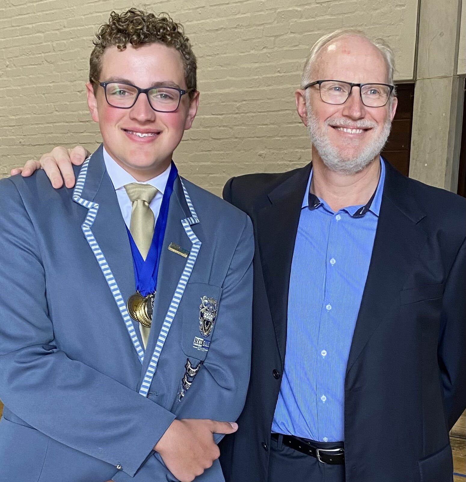 Teenage son in school blazer with medals beside his proud father