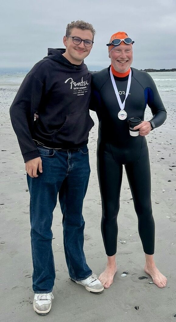 Grown son on the beach with his father in a wetsuit after an ocean swim