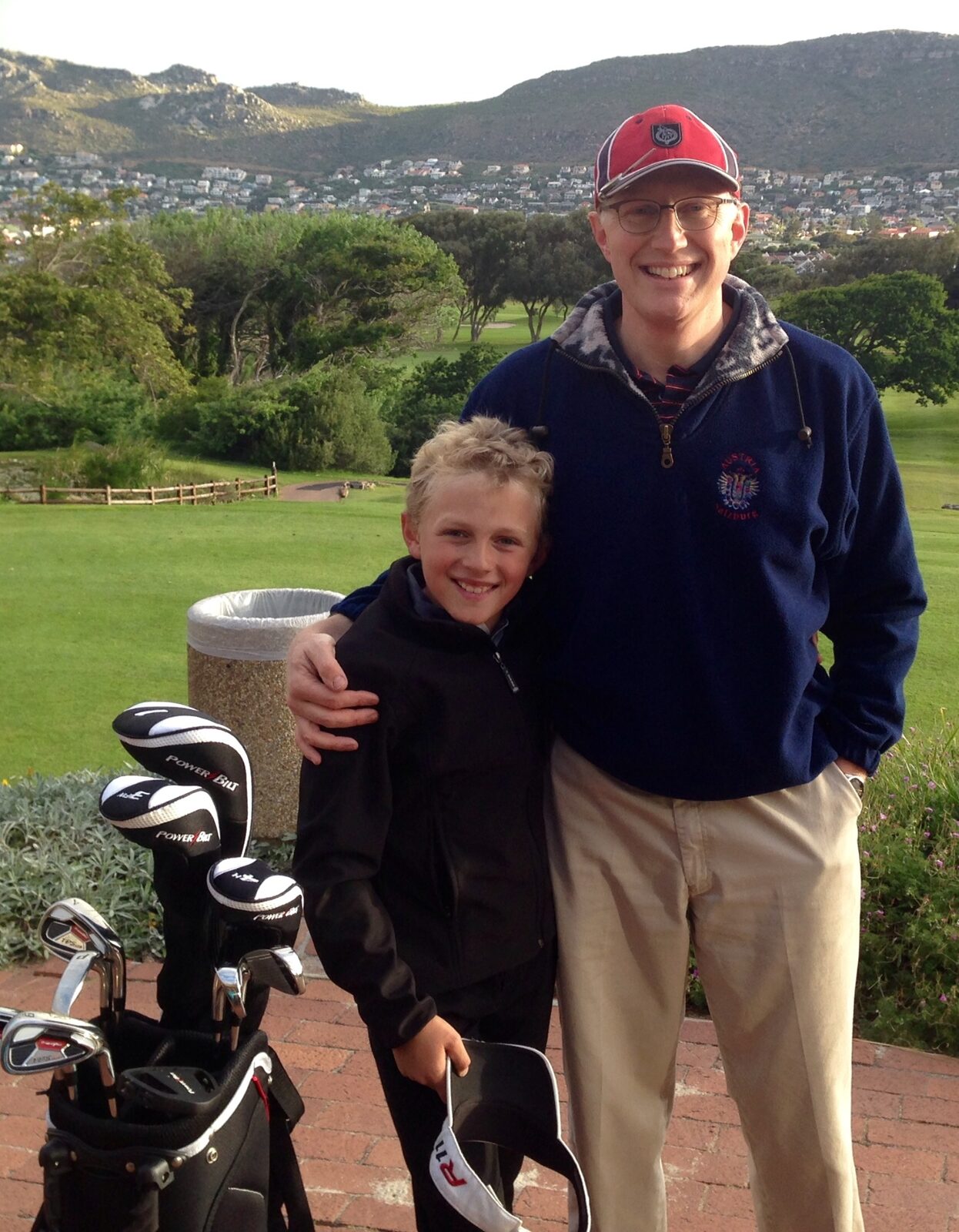 Father with arm around his young son on a golf course with mountains behind