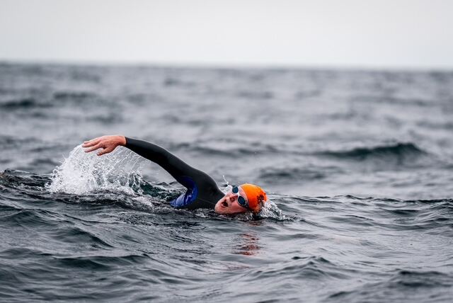 Open-water swimmer mid-stroke in a steady rhythm across grey swells